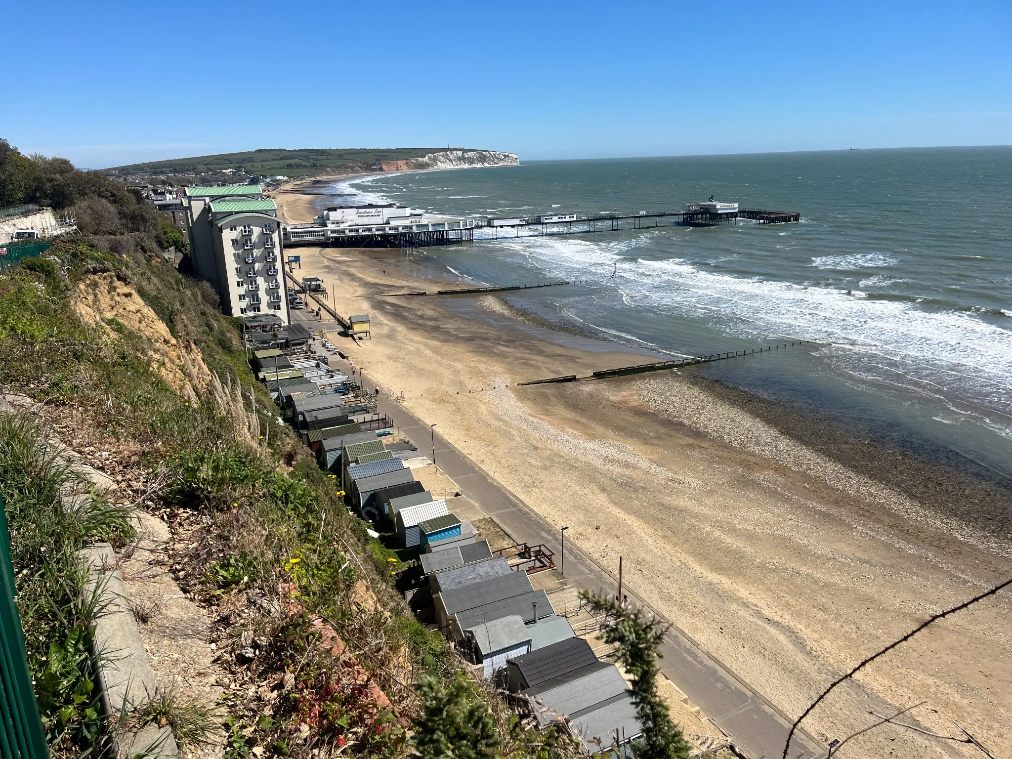 Beach huts lining Sandown Bay below the cliff path, with Sandown Pier and Culver Cliff beyond