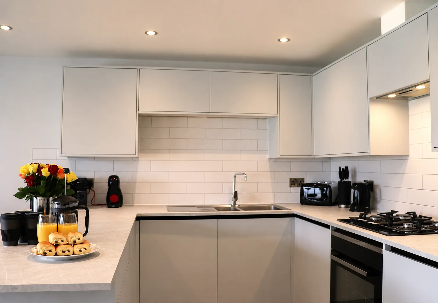 Modern light-grey fitted kitchen prepared with juice, pastries and flowers