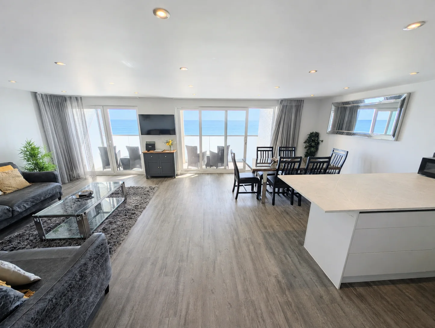Open-plan apartment with lounge, dining area, kitchen and sea beyond the frosted balcony glass